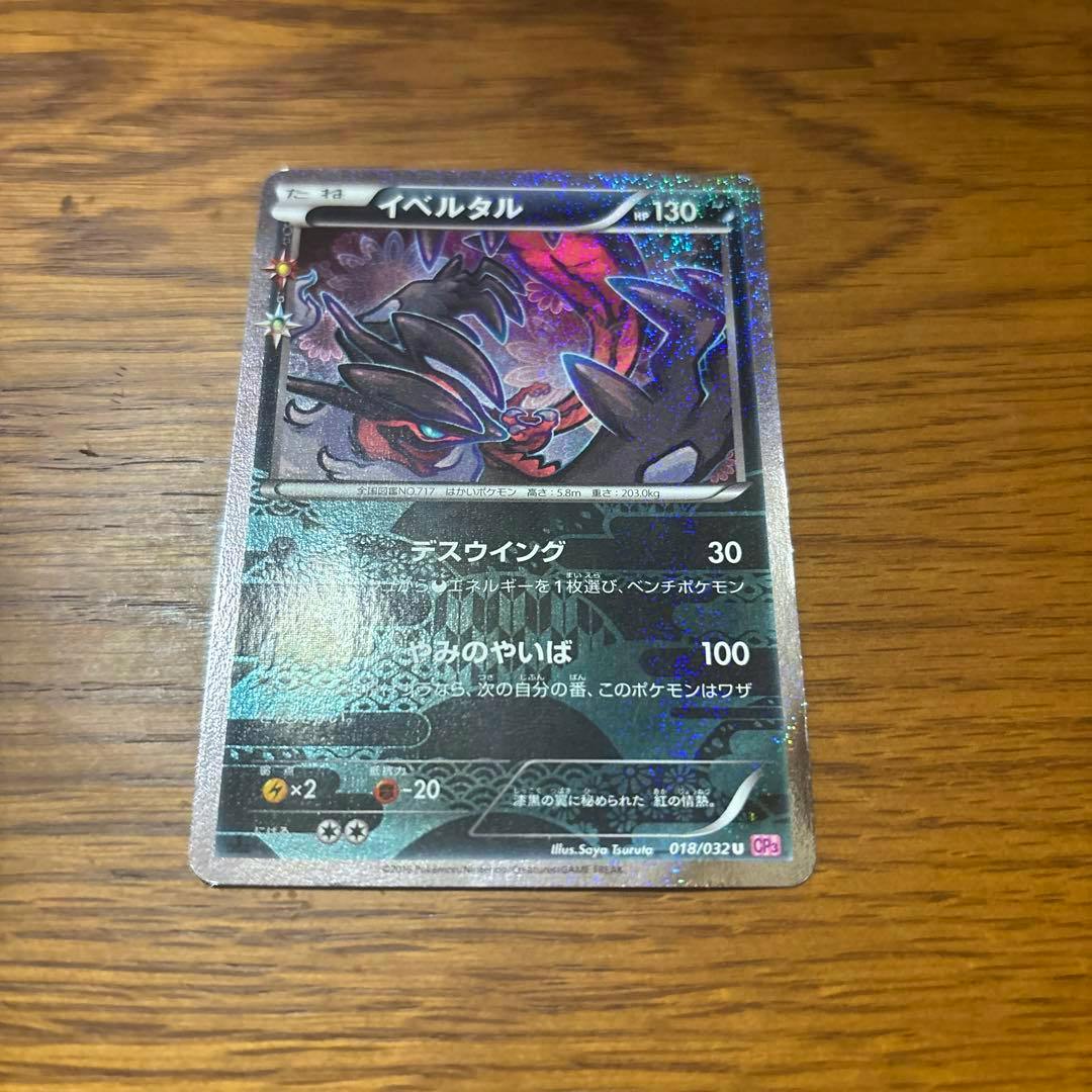 Photograph of the front (Japanese) side of the Yveltal Pokémon trading card with holographic foil, lying on a wooden surface.