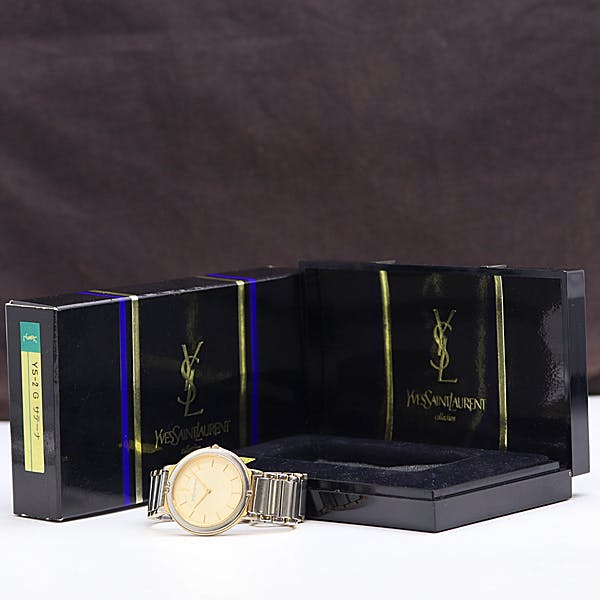 An Yves Saint Laurent women's wristwatch with an ivory dial shown in front of its black Yves Saint Laurent presentation box.