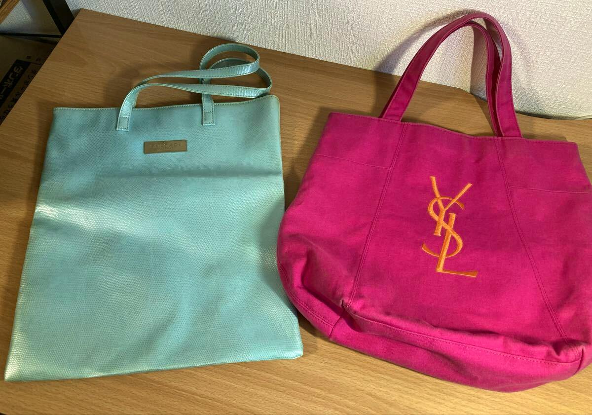 Two tote bags on a wooden surface: a pink Yves Saint Laurent canvas tote with a yellow YSL logo and a light turquoise Bulgari tote.