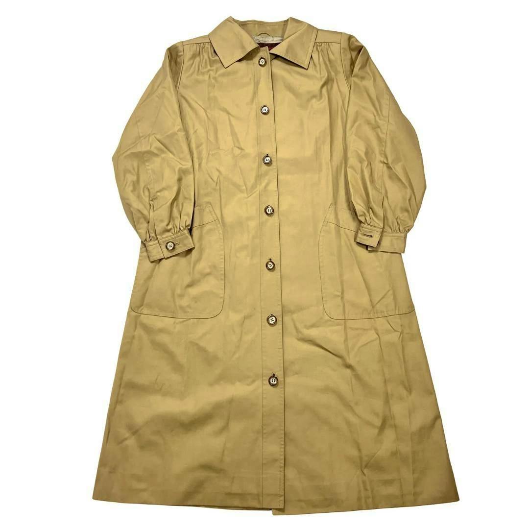 Beige women's trench coat laid flat showing the front with buttons, cuff straps, and front patch pockets.