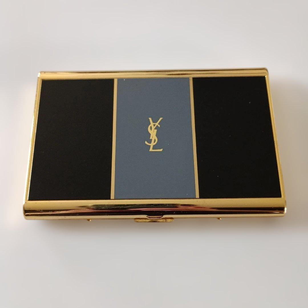 Yves Saint Laurent business card case with gold trim and black and gray panels on a white background.