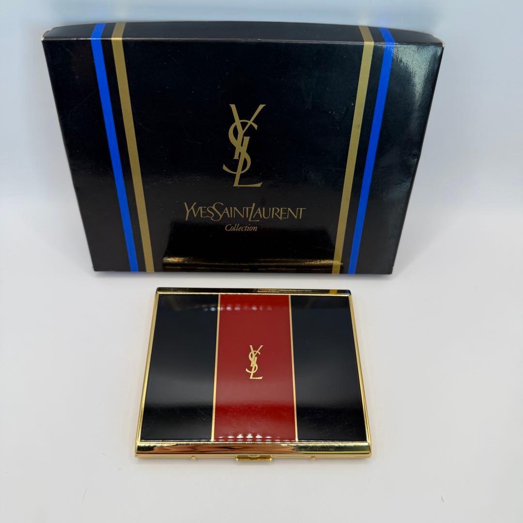 Yves Saint Laurent cigarette/card case with black and red panels and a gold YSL logo placed in front of its black Yves Saint Laurent box.