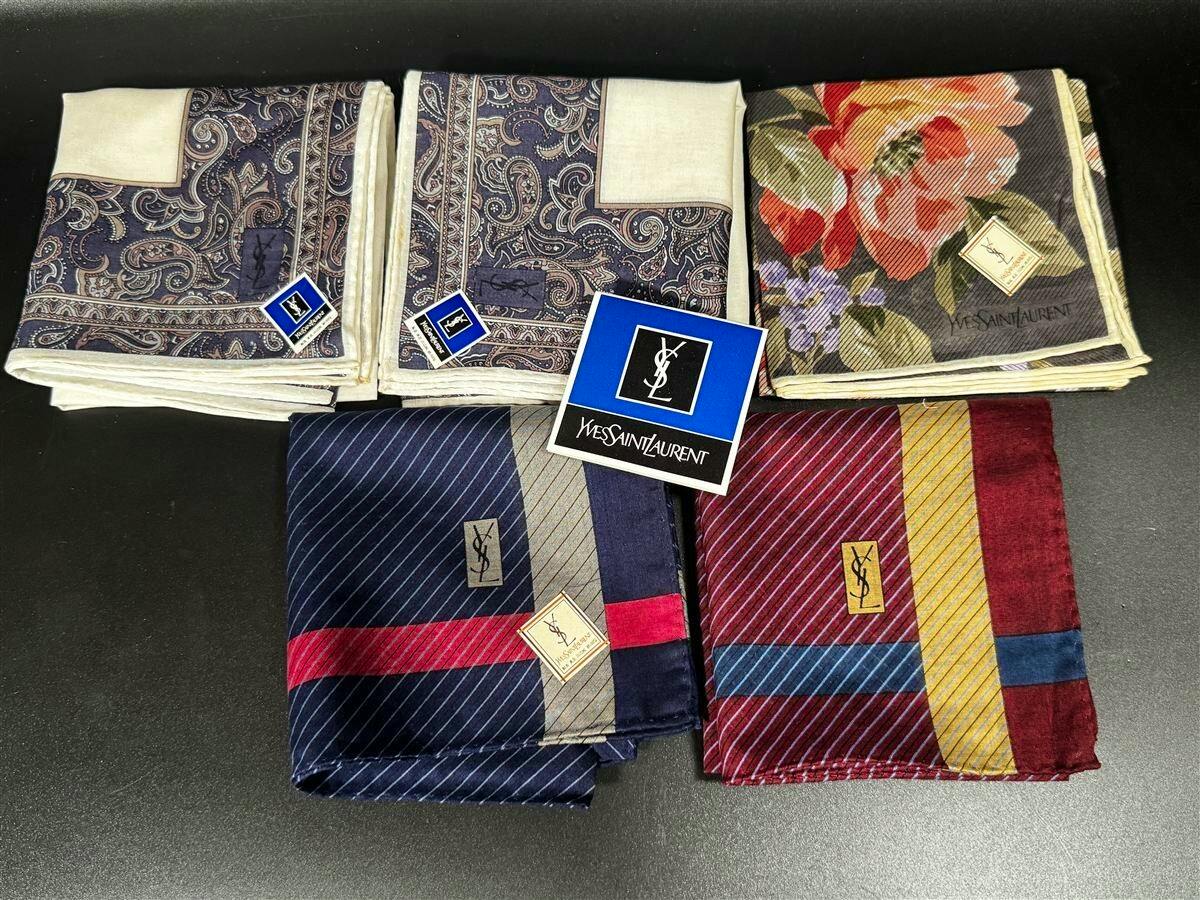 Five folded Yves Saint Laurent silk handkerchiefs with paisley, floral, and striped designs on a dark background, with a YSL label visible.