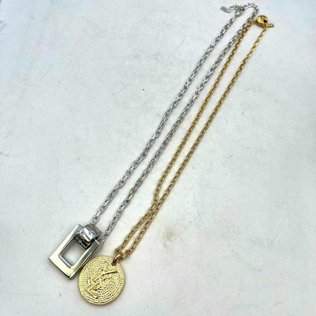 Two metal Yves Saint Laurent necklaces laid flat, one gold chain with a round YSL medallion and one silver chain with a rectangular pendant.