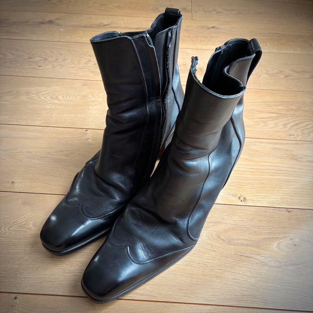 Angled front view of a pair of Yves Saint Laurent rive gauche black leather boots on a wooden floor.