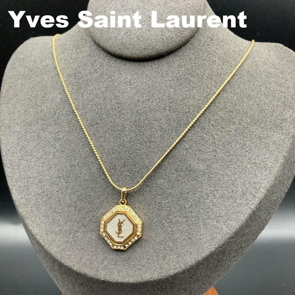 Gold-tone Yves Saint Laurent necklace with an octagonal rhinestone-studded pendant bearing a YSL logo displayed on a gray necklace bust.
