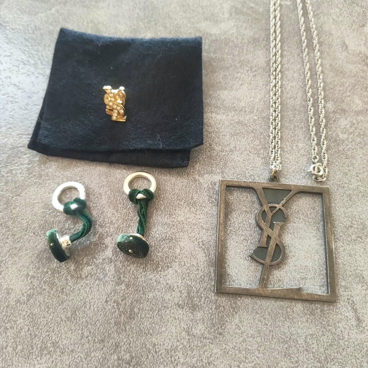 Yves Saint Laurent pendant necklace with YSL logo, a pair of cufflinks, and a pin badge displayed on fabric.