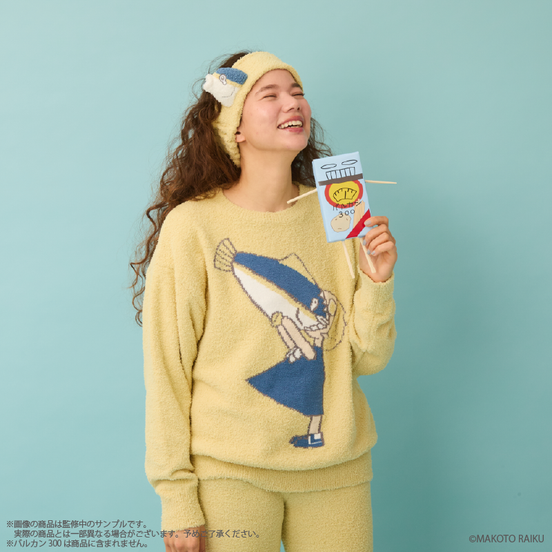 Model wearing a yellow fluffy roomwear pullover and matching pants with a printed character design, posing against a light blue background.
