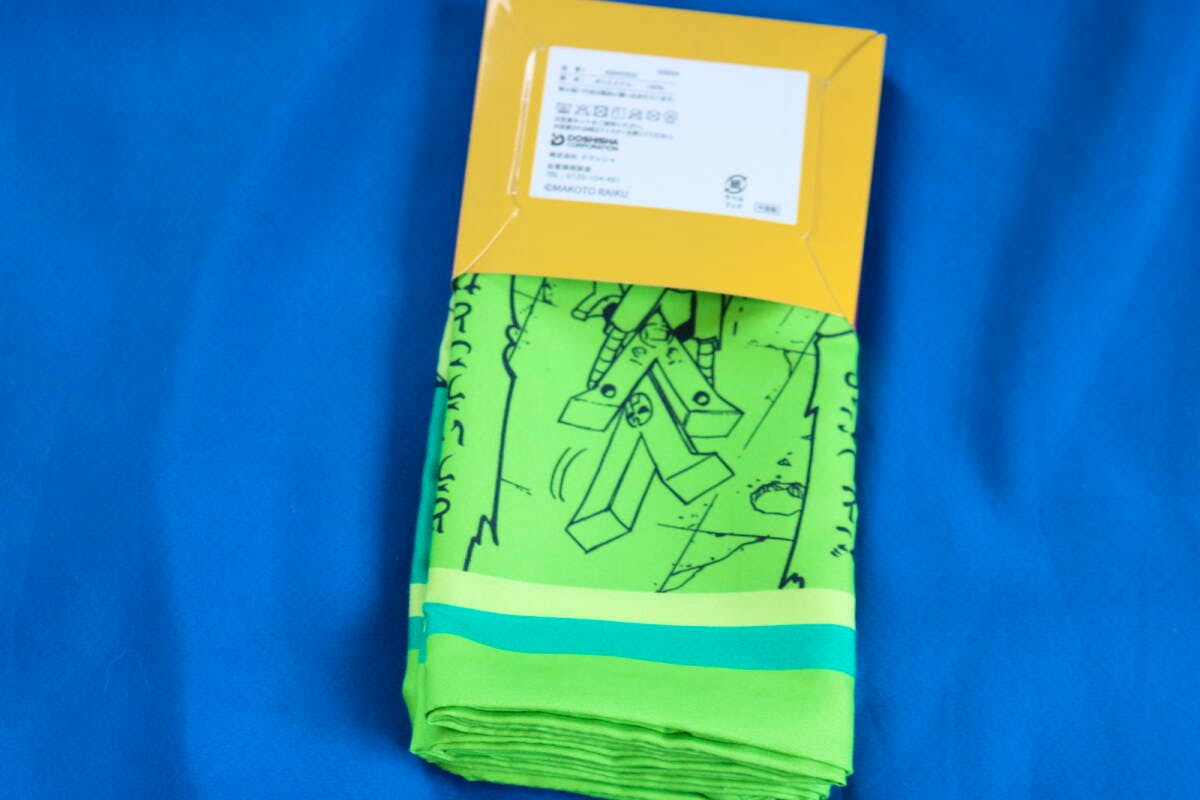 A folded green pillow cover with printed design partially visible inside yellow packaging on a blue background.