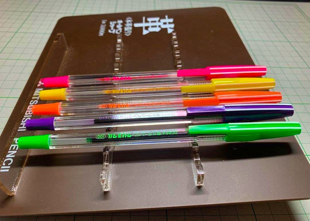 Five Zebra fluorescent crystal ballpoint pens with pink, yellow, orange, purple, and green caps arranged on a brown display.