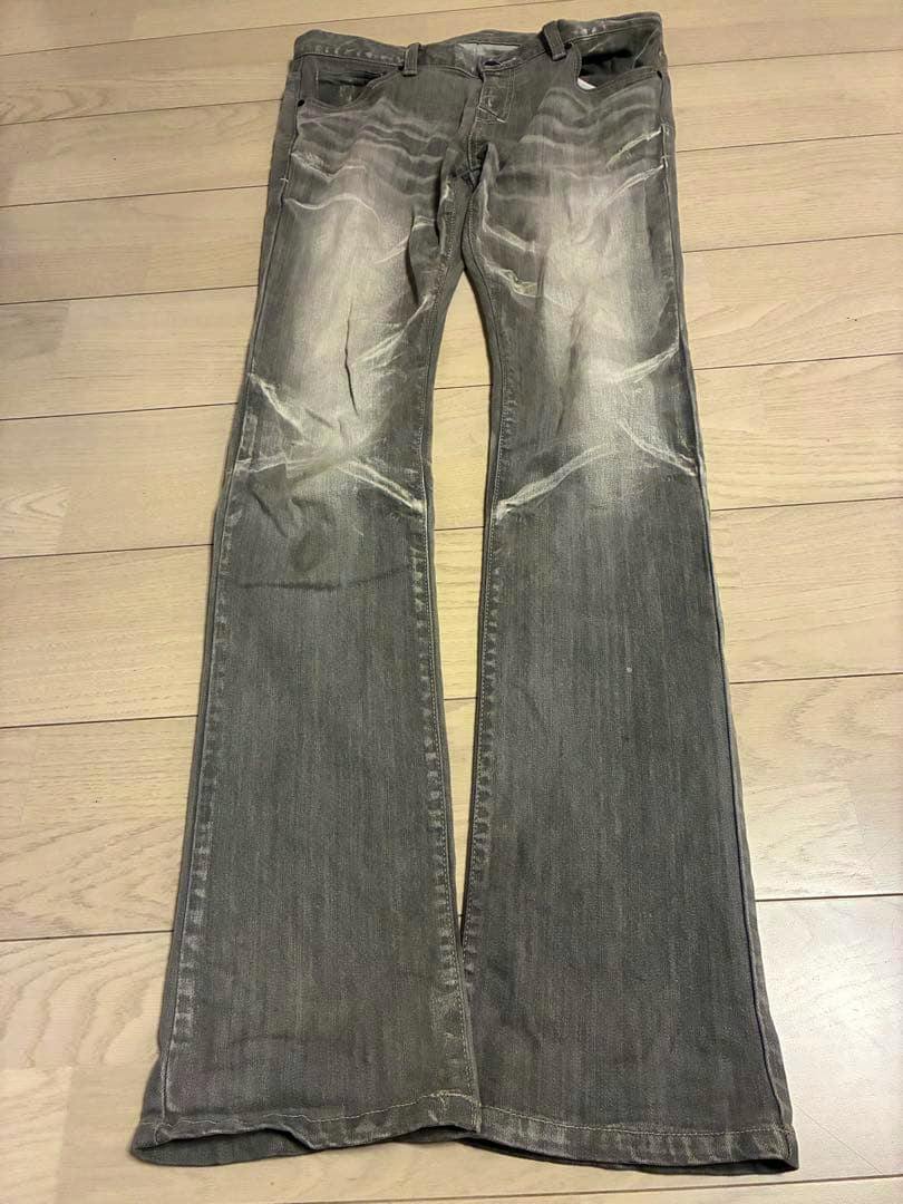 Front view of gray men's denim jeans with whisker wrinkles laid flat on a wooden floor.