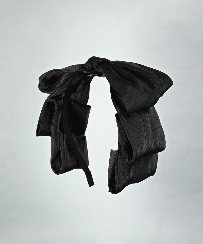 Black ribbon decorative hairband with a large bow and layered ribbon details suspended against a plain gray background.