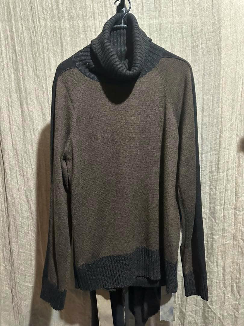 Front view of a Ziggy chen baby cashmere turtleneck sweater hanging on a hanger against a fabric backdrop.