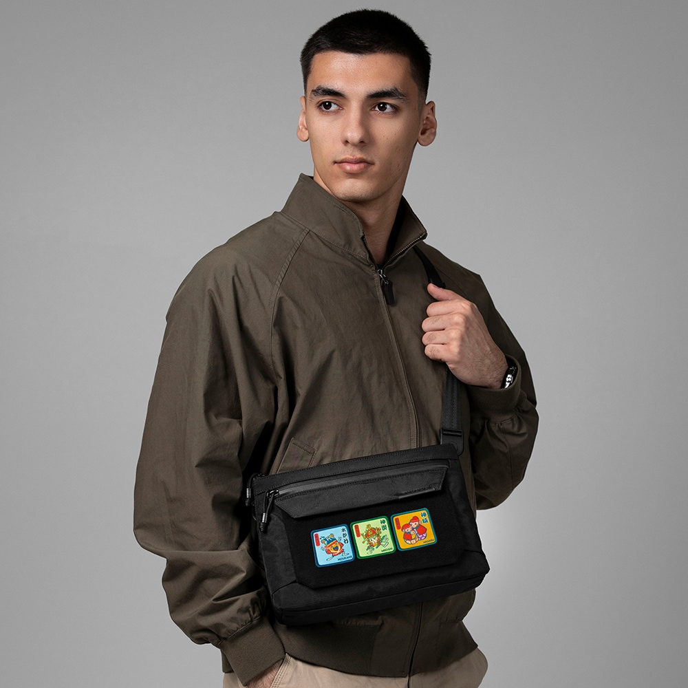 A model wearing a black polyester zip pouch crossbody that displays three colorful Matsuri series patches on the front.