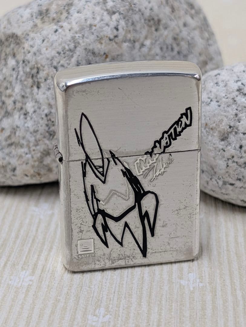 Front view of the metal Zippo lighter case (insert removed) showing a black stylized graphic and surface scratches.