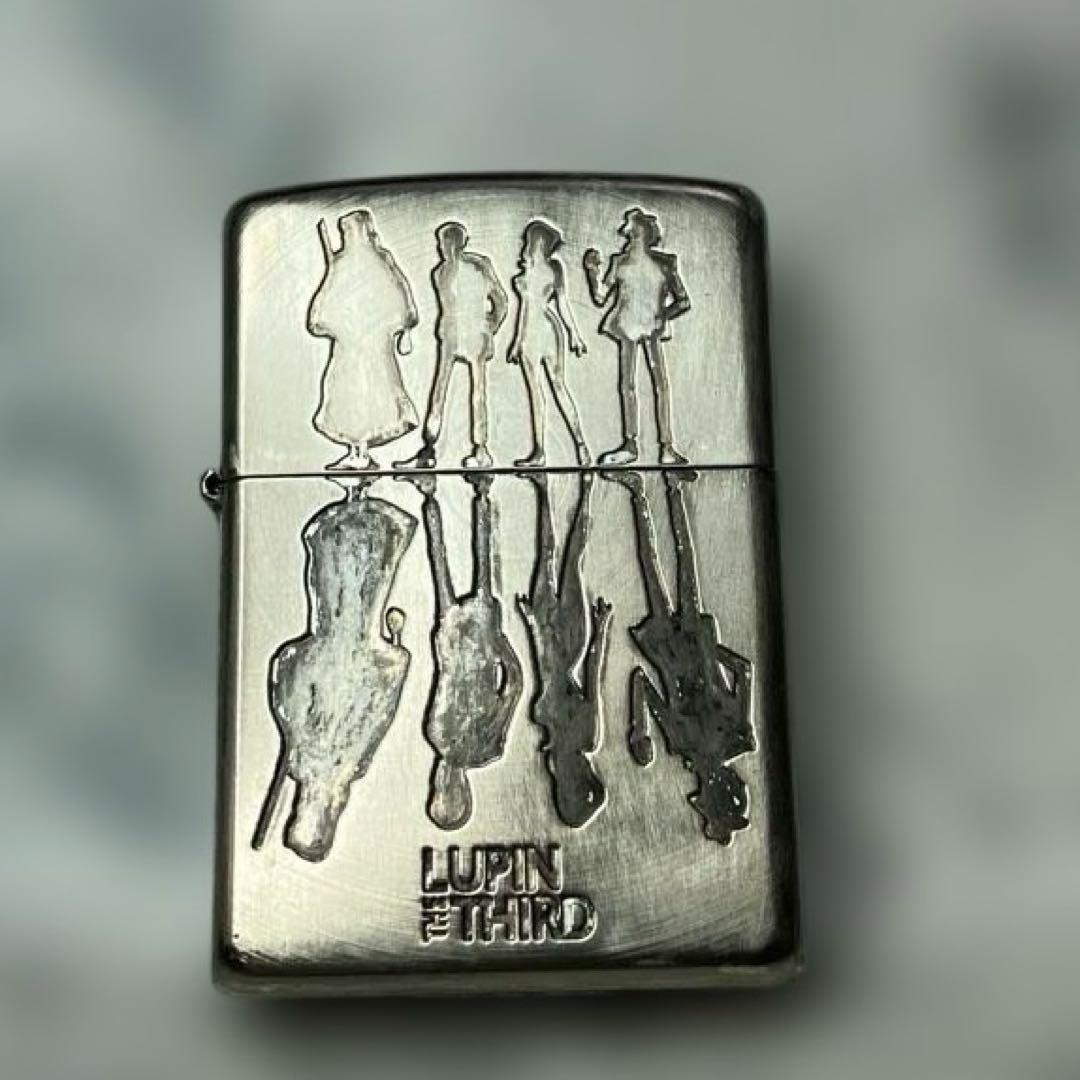 Silver Zippo lighter case with engraved Lupin III character silhouettes and "LUPIN THE THIRD" text on the front.