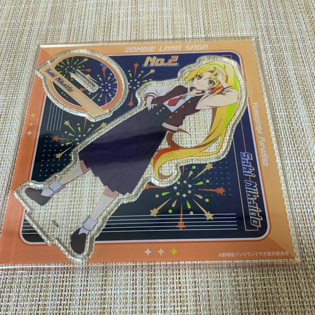 Packaged acrylic stand showing the character Saki Nikaidou from Zombieland Saga on a decorative backing card.