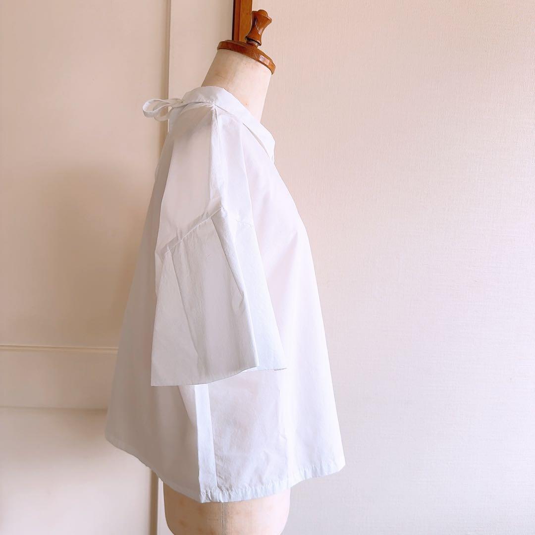 Side view of a white women's blouse with ruffle sleeves displayed on a dress form, showing the flared sleeve and collar with a tied back ribbon.
