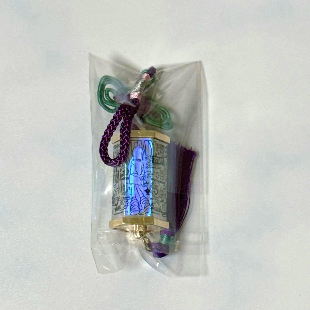 Packaged acrylic omikuji keychain with a purple braided cord and tassel inside clear plastic.