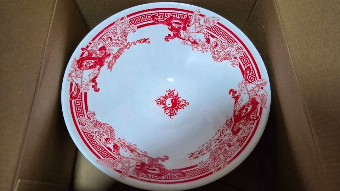 Top-down view of the ramen bowl showing red dragon pattern inside, placed in a cardboard box.
